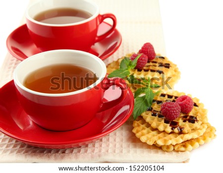 Cups of tea with cookies and raspberries isolated on white