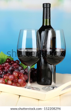 Ripe grapes, bottle and glasses of wine on tray, on bright background