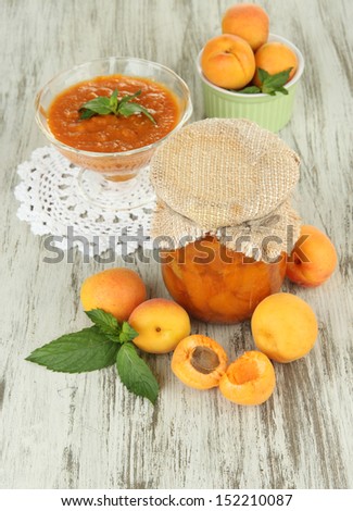 Apricot jam in glass jar and fresh apricots, on wooden background