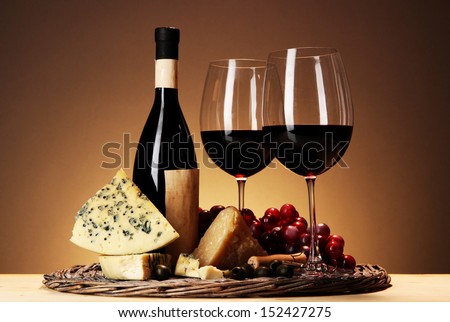 Refined still life of wine, cheese and grapes on wicker tray on wooden table on beige background