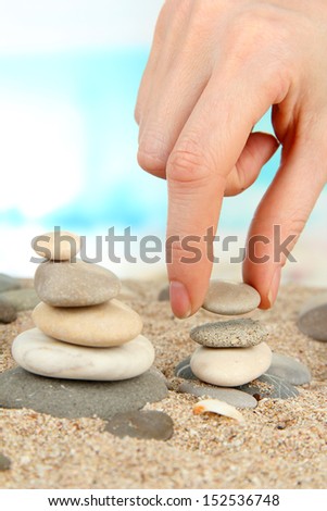 Hand builds tower of sea stones on sand on bright background
