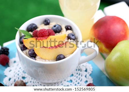Oatmeal in cup with berries on napkin on table on grass background