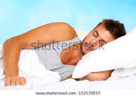 Handsome young man in bed, on bright background, close-up