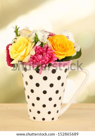 Beautiful bouquet of bright flowers in color mug, on wooden table, on bright background
