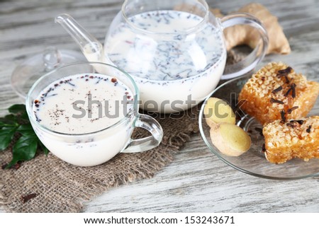 Teapot and cup of tea with milk and spices on sackcloth of wooden table
