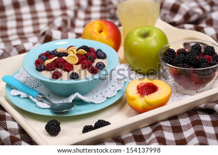 Oatmeal in plate with berries on napkins on wooden tray on bad