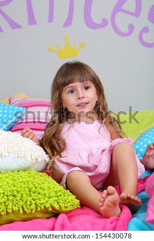 Little girl sitting on bed in room on grey wall background