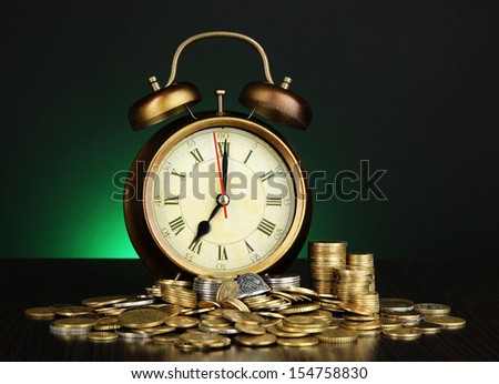 Antique clock and coins on wooden table on dark color background