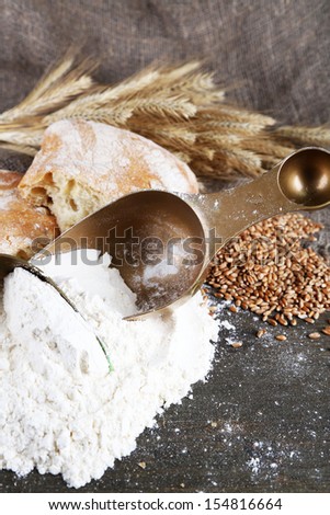 The wholemeal flour in scoops on wooden table on sackcloth background