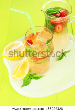 Basil lemonade with strawberry in  jug and glass, on color wooden background