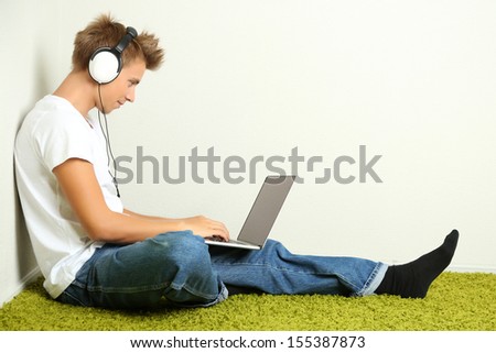 Young Man Relaxing On Carpet And Listening To Music, On Gray Wall Background