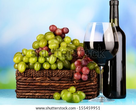 Ripe green and purple grapes in basket with wine on wooden table on natural background