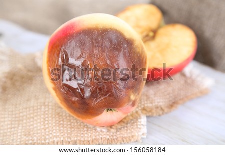 Rotten apples on wooden board on sackcloth