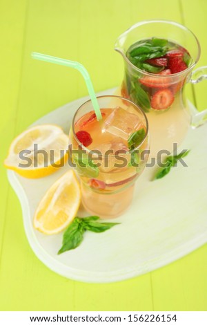 Basil lemonade with strawberry in  jug and glass, on color wooden background