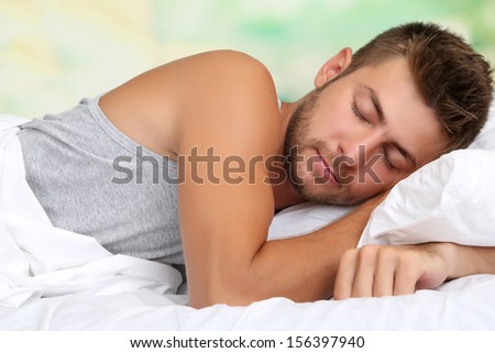 Handsome young man in bed, on bright background, close-up