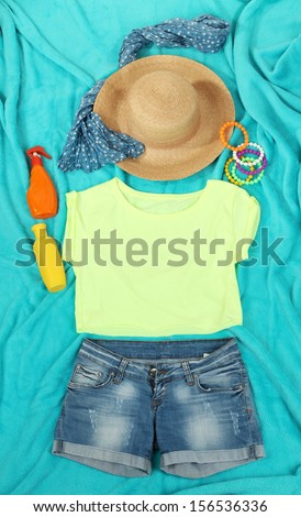 Top, shorts and beach items on bright blue background