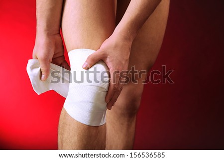 Young man with elastic bandage on knee, on red background