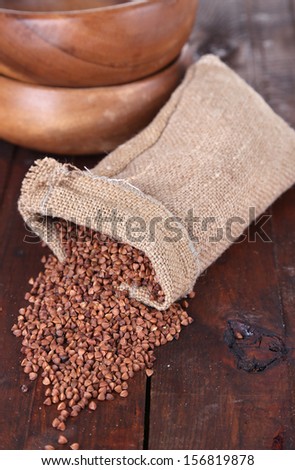 Cloth bag with buckwheat groats and bowls on wooden background