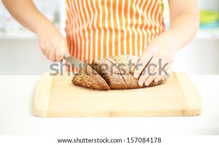 Woman slicing bread with sesame seeds on chopping board, close up