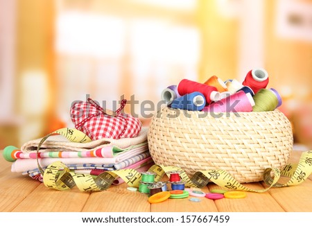 Wicker basket with accessories for needlework on wooden table, on bright background