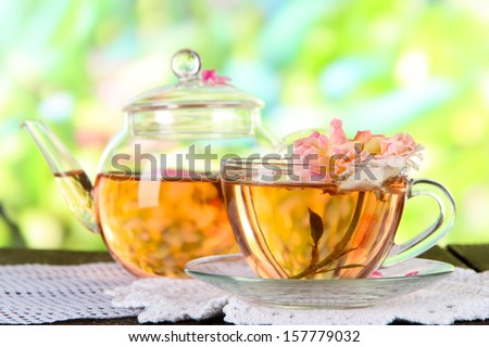 Kettle and cup of tea from tea rose on napkin on wooden table on nature background