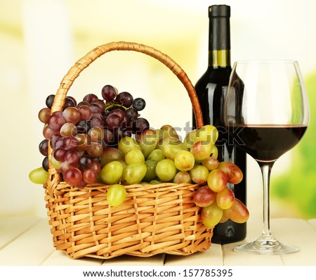 Ripe grapes in wicker basket, bottle and glass of wine, on light background