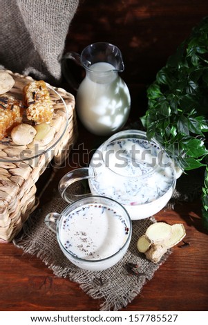 Teapot and cup of tea with milk and spices on sackcloth of wooden table on bright background