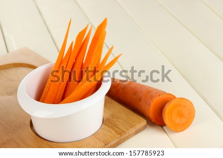 Bright fresh carrot cut up slices in bowl on wooden table close-up