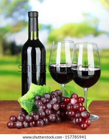 Ripe grapes, bottle and glasses of wine on bright background