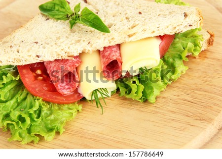 Tasty sandwich with salami sausage and vegetables on cutting board,  close-up