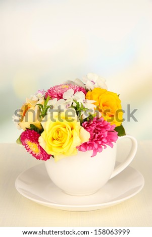 Beautiful bouquet of bright flowers in color mug, on wooden table, on  light background