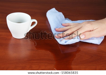 Hand wiping wooden surface with blue rag and cup of coffee