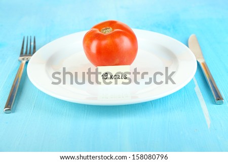 Calorie content of tomato on plate on wooden table close-up