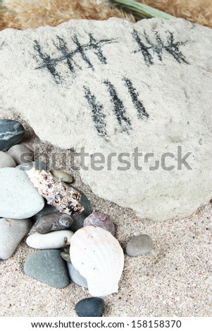 Counting days by drawing sticks on stone with stones and shells on sand background