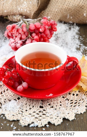 Still life with viburnum  tea in cup, berries and snow, on  wooden background