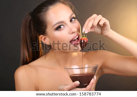 Portrait of beautiful young girl with strawberry in chocolate on brown background