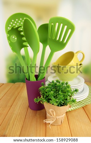 Plastic kitchen utensils in stand with clean dishes on table on bright background