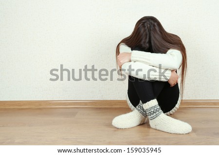 Sad woman sitting on floor near wall