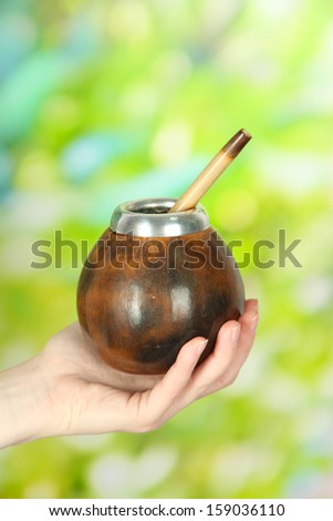Woman hand giving calabash and bombilla with yerba mate, on nature background
