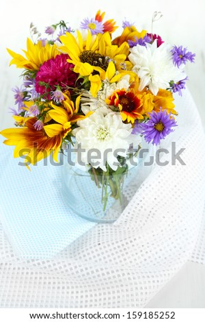 Bouquet of wild flowers in glass vase on light background