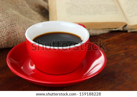 Cup of coffee and book on wooden table on sackcloth background