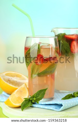 Basil lemonade with strawberry in  jug and glass, on wooden table, on bright background