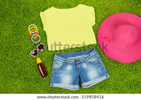 Top, shorts and beach items on bright green background