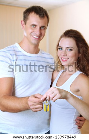 Young couple with keys to your new home on room background