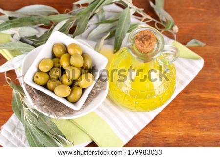 Olives in bowl and oil with branch on napkin on wooden board on table