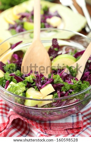 Fresh vegetable salad in bowl and plate on napkin on wooden table close-up