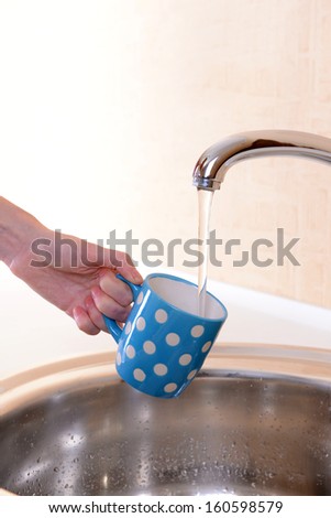 Hand holding  cup of water poured from  kitchen faucet