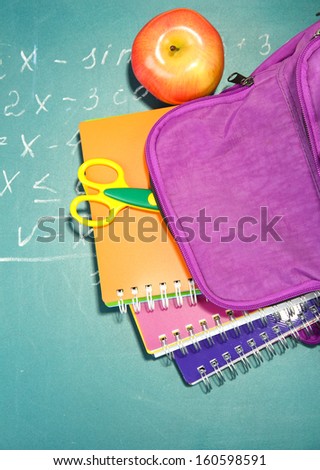Purple backpack with school supplies on green desk background