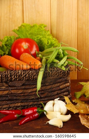 Different vegetables in basket with yellow leaves on table on wooden background