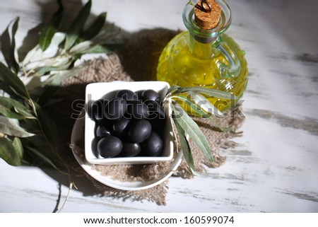 Olive oil and olives in bowl on sackcloth on wooden table